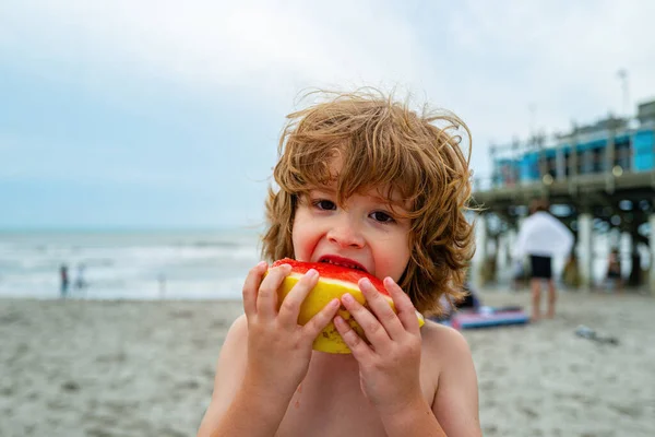 Un bambino mangia l'anguria. Ragazzo carino mangiare anguria mentre in piedi sulla spiaggia estiva . — Foto Stock