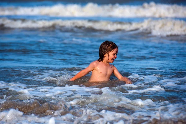 Niño feliz disfruta de la vida en la playa de verano. Lindo niño que se divierte en la playa de arena en verano. Océano o mar wawes en el fondo . —  Fotos de Stock