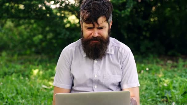 Divertido barbudo trabajando con un portátil en el parque. freelance o teletrabajo, concepto de chat en línea . — Vídeo de stock