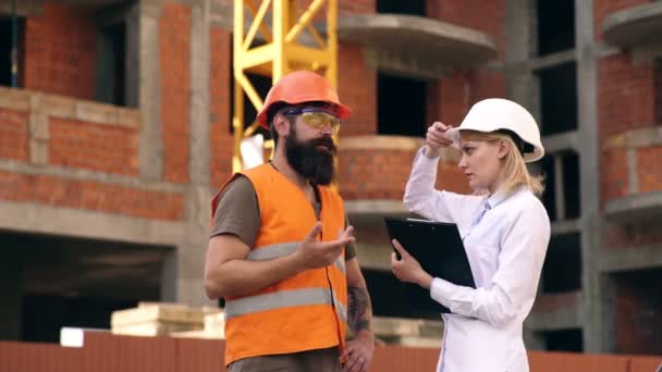 Zwei Ingenieure besprechen mit dem Bauunternehmer den Zeitpunkt der Bauarbeiten. Die Arbeit der Ingenieure auf der Baustelle. Konzept des Bauens. — Stockvideo