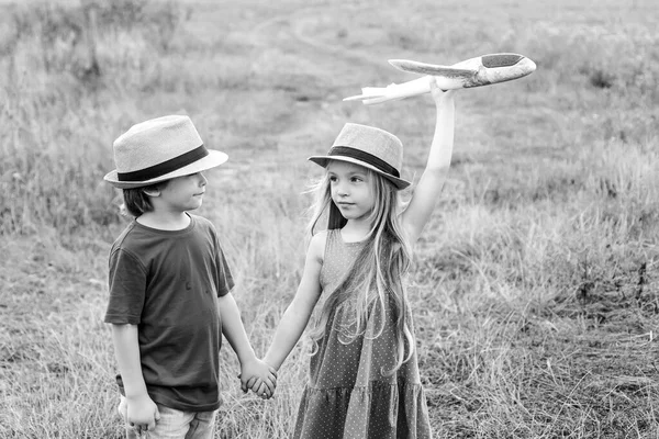 Hijitos, hija e hijo juegan y sueñan con volar. Cuidado de niños. Lindos niños - hija e hijo jugando con el avión de juguete en el prado en tono de color vintage . — Foto de Stock