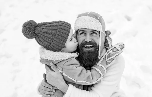 Sohn umarmt seinen Vater im Winterurlaub. Vater und kleiner Sohn spielen zusammen im Freien. Glückliches Kind spielt mit Schneeball vor weißem Winterhintergrund. — Stockfoto