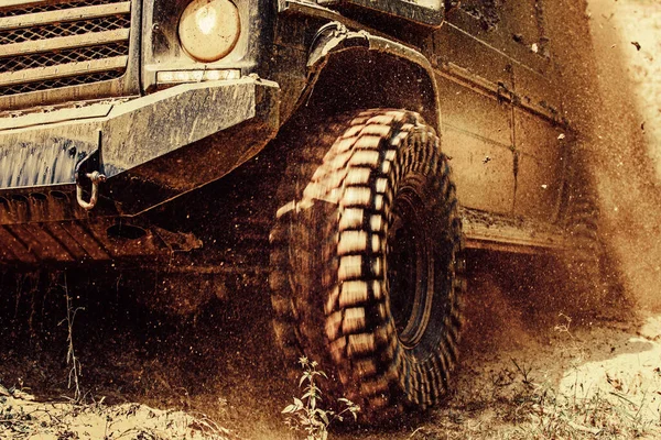 Geländewagen, der aus einem Schlammloch kommt. Blick von unten auf großes Offroad-Autorad auf Landstraße und Bergkulisse. Offroad auf der Bergstraße. — Stockfoto