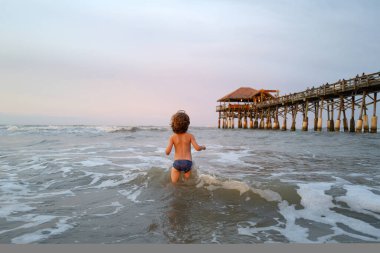 Küçük çocuk mavi denizde dalgalarla oynuyor. Seyahat ve macera konsepti.