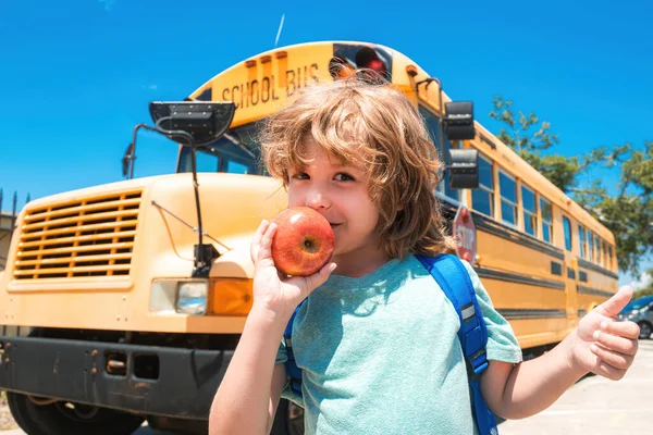 Kind aus der Grundschule mit Tasche im Schulbus. Schüler vor dem Schulbus mit Apfel. — Stockfoto