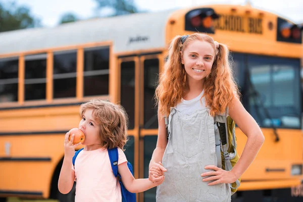 Schulbus und glückliche Kinder. Porträt eines glücklichen Geschwisterpaares, das zusammen vor dem Schulbus steht. — Stockfoto