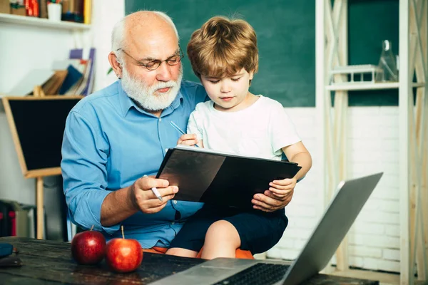 Old and Young. Happy cute clever boy and old tutor with book. Educational process. Family generation and relations concept. Educational process. Grandfather with grandson learning together.