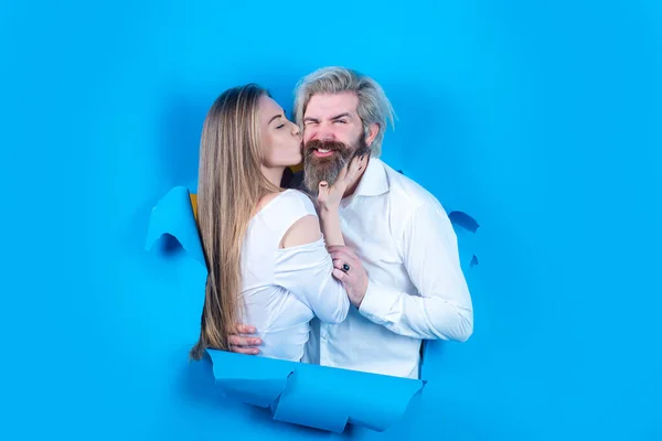 파란 배경에 행복 한 커플이네요. 종이 사이로 키스하는 젊은 커플. 놀란 남녀 가벽을 내다보고 있다. — 스톡 사진