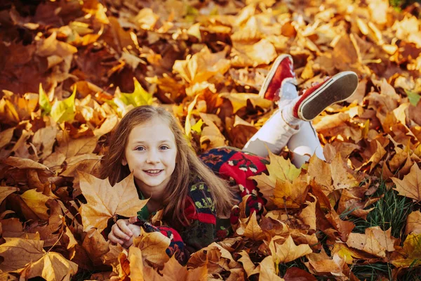 Mädchen auf Blättern liegend. Entzückendes kleines Mädchen mit Herbstblättern im Schönheitspark. Lustige Kinder im herbstlichen Park. Kleines Mädchen im Herbst orange Blätter. — Stockfoto