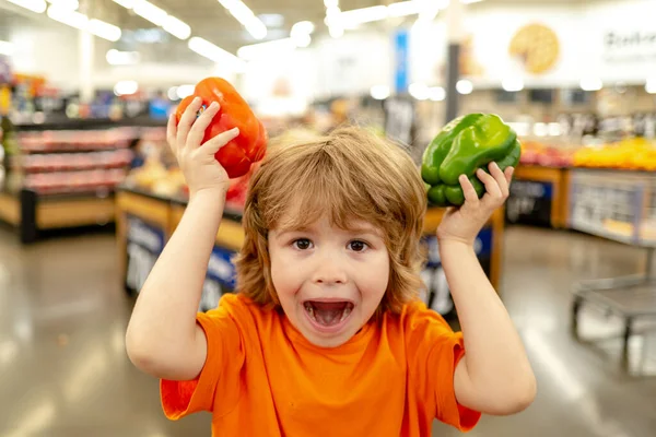 Carino il bambino in un negozio di alimentari o in un supermercato che sceglie carote biologiche fresche. Stile di vita sano per giovani famiglie con bambini — Foto Stock