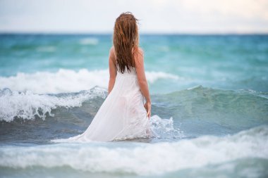 Doğada güzel deniz ve mavi gökyüzü olan genç bir kadın. Yaz tatili ve seyahat konsepti. Hayal gücü ve hayal gücü. Şehvetli kız mavi denizde dalgalarla oynuyor..