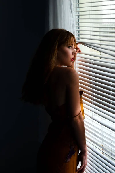 Krásná paní u okna. Smyslná mladá žena. Roztomilá dívka v krásné pozici. Interiér hotelového pokoje s velkými okny. — Stock fotografie