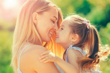 Mutlu anne ve kızın portresi. Anne ve çocuğun gülümseyen yüzlerini kapat. Mutlu gülümseyen anne gün batımında küçük kızına sarılıyor. Anneler Günün kutlu olsun. Ebeveynlik konsepti.