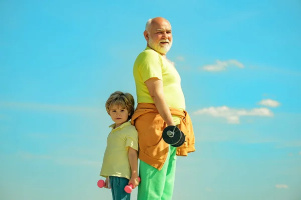 Exercice sportif pour les enfants. Grand-père et petit-fils pratiquent des exercices d'haltères à l'extérieur. Levage d'haltères. Garçon fait des exercices pour développer les muscles. — Photo