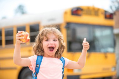 Çocuk okul otobüsüne biniyor. Elinde olumlu bir jest olan, gülümseyen ve mutlu bir çocuk. Evde eğitim.
