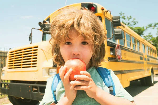 Возвращайся в школу. Школьник перед школьным автобусом ест яблоко . — стоковое фото