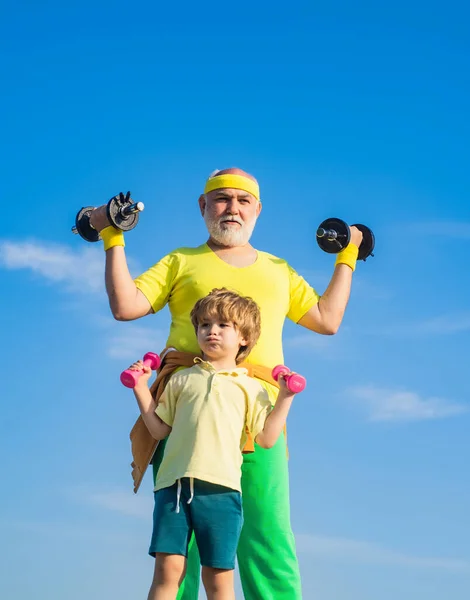 体育和培训概念。家庭运动。爷爷和儿子在做运动。抚养一个哑铃的孩子有趣的老男人和带哑铃的小孩. — 图库照片