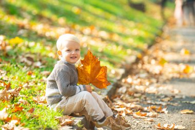 Sonbahar yapraklarıyla oynayan tatlı bir çocuk. Sonbahar doğa arka planında kalın ceketli şirin bir çocuk. Mutlu çocuk sonbaharda dışarıda rüya görür. Rüya gören çocuklar..