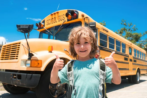 Gelukkig schoolkind. Kind van de basisschool met tas op schoolbus achtergrond. Succes teken doet positief gebaar met de hand, duimen omhoog glimlachend en gelukkig. — Stockfoto