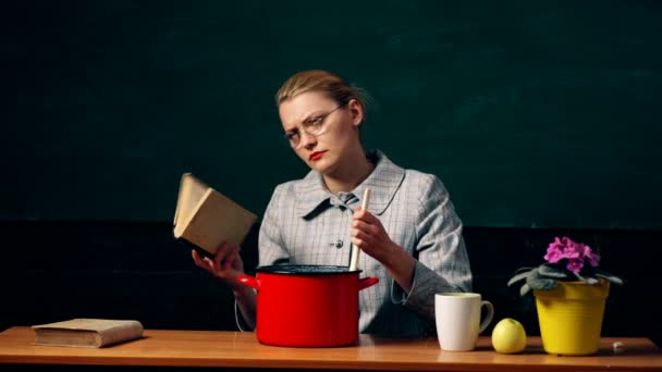 テーブルの面白い先生は、緑の学生ボードの背景にクレヨンとペンを鍋に投げます。脳のための食品. — ストック動画