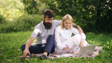 Genç çift parkta sınavlara hazırlanıyor. Adam parktaki çimenlikte dizüstü bilgisayarla çalışan kıza sarılıyor. Parktaki çimlerin üzerinde otururken arkadaşlar gülümsüyor. Açık hava eğitimi kavramı.
