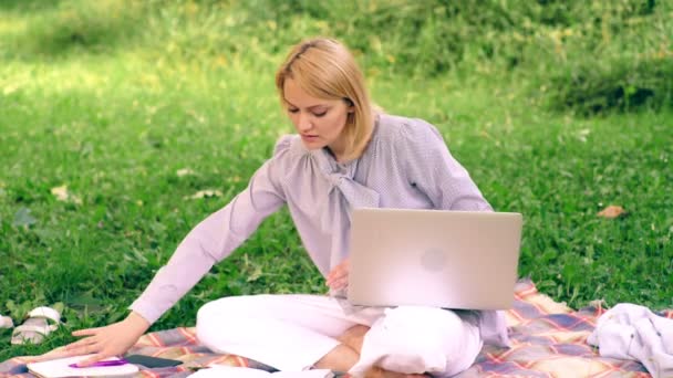 Chica con cuaderno, sentada en el césped del parque. Estudiante se prepara para el examen en el parque. El concepto de educación al aire libre . — Vídeos de Stock