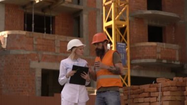 İki mühendis inşaat alanında bir inşaat planını tartışıyorlar. Beyaz kasklı bir kadın ve sakallı bir adam şantiyede konuşuyor. İnşaat kavramı.
