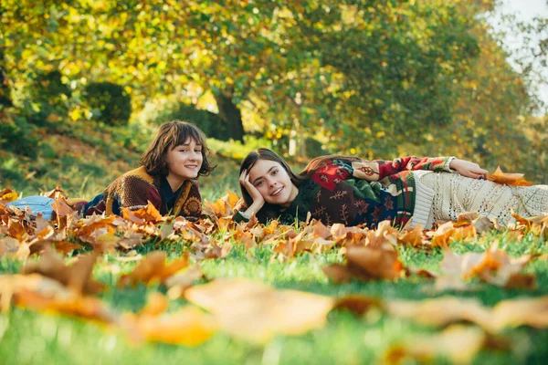 Duas belas mulheres jovens desfrutando da natureza em um dia ensolarado de outono. Retrato de duas mulheres deitadas ao ar livre no parque de outono. Meninas deitadas em folhas . — Fotografia de Stock