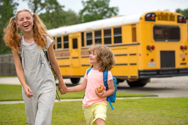 Glückliches Foto von zwei glücklichen Kindern, die aus den Fenstern eines gelben Schulbusses schauen. Viel Platz für Text. Bruder und Schwester stehen gemeinsam vor Schulbus. — Stockfoto