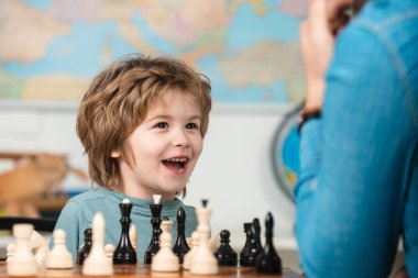 Çocuk satranç okulu. Neşeli gülümseyen küçük çocuk masada oturuyor ve akşam keyfi ile satranç oynuyor..