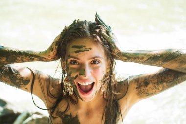 Deli kadın dışarıda çamurda oynarken gülüyor ve elleriyle yüzüne çamur sürüyor..