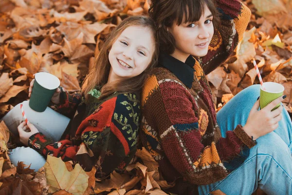 Close up retrato de sorrir menina bonita jovem com a irmã no tempo de outono. Retrato de duas meninas bonitas ao ar livre no outono. Retrato de irmãs. Tempo quente e ensolarado. Conceito de queda . — Fotografia de Stock