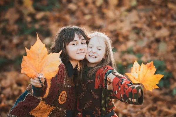 Vidám lányok az őszi parkban. Lány modell az őszi szezonban. Közelkép egy mosolygós fiatal csinos lányról a nővérével ősszel. Gyönyörű nővérek az őszi háttérben. — Stock Fotó