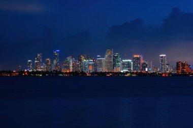 Skyline City Miami, deniz okyanusunu aydınlatıyor. Günbatımı, şehir merkezindeki şehir manzarası, mimari gökdelenler, alacakaranlık panoraması. Miami.