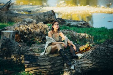Yetişkin bir kadın açık hava parkında odunların üzerinde rahatça oturuyordu. Romantik bir kadının sanat eseri. Kadın modası. Mesaj için yer. Doğal makyajlı güzel kız portresi..