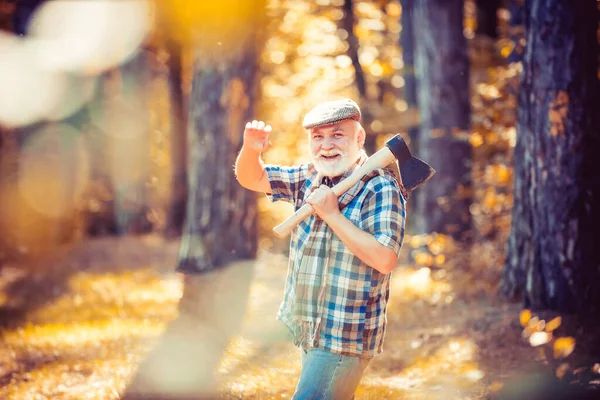 Viejo barbudo al aire libre. Retrato de un anciano con barba. Viejo sonriente con hacha. Senderismo en madera profunda. Un gracioso guardabosques en el bosque. Anciano paseo masculino en el bosque . — Foto de Stock