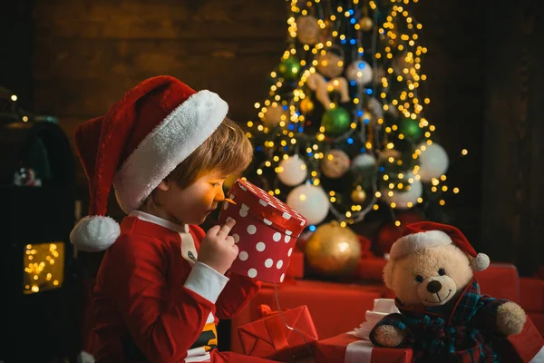 クリスマスのギフトボックスと幸せな小さな笑顔の男の子。休日の概念。小さな子供はサンタの服を着ている. — ストック写真