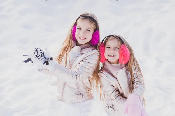 Due adorabili ragazze si divertono insieme nel bellissimo parco invernale. Ritratto invernale per bambini. Abbigliamento invernale per neonati e bambini piccoli. Bambini in Winter Park a giocare palle di neve. — Foto Stock