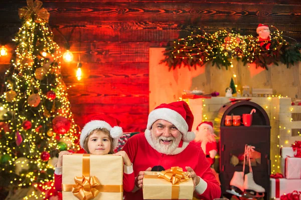 Pai Natal pequeno engraçado e filho segurando saco com presentes. Papai Noel avô e neto. Menino criança brincar com o verdadeiro Papai Noel perto da árvore de Natal. — Fotografia de Stock