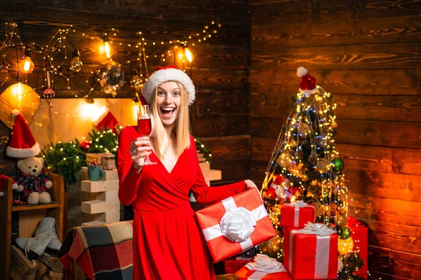 Fille de Noël en robe rouge avec champagne. Santa femme posant sur fond de bois vintage. Femme en robe de soirée sur fond d'arbre de Noël à la maison. Nouvel an réveillon célébrant concept. — Photo