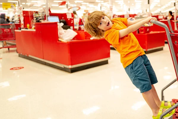 Criança engraçada segurando saco de compras cheio de vegetais frescos no supermercado ou loja. — Fotografia de Stock