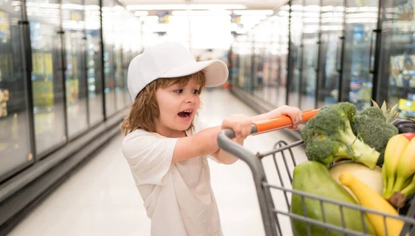 La venta, el consumismo y el concepto de la gente - niño feliz con comida en el carrito de la compra en la tienda de comestibles . —  Fotos de Stock