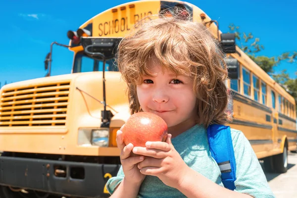 Schüler vor dem Schulbus beim Apfel essen. Kind aus Grundschule mit Tasche im Schulbus unterwegs. — Stockfoto