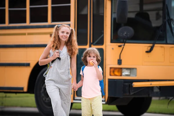 Grundschüler im Schulbus. Wenig bereit zum Studium. Glückliches Geschwisterpaar steht gemeinsam vor Schulbus. — Stockfoto