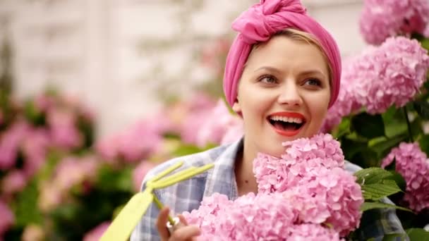 Mujer americana con un pañuelo rosa cuida hortensias. Chica en jardín patio trasero. — Vídeos de Stock