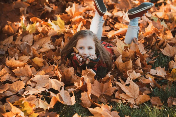 Söt liten flicka i höstparken. En liten flicka i löv. Glada barn skrattar och leker löv på hösten utomhus. Vacker glad flicka som har roligt i höstparken bland fallna blad. — Stockfoto