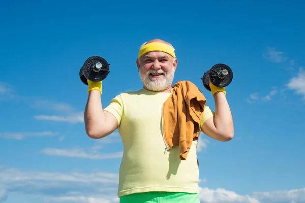 Sportivo anziano che si esercita con il sollevamento di manubri su sfondo cielo blu. Isolato, spazio di copia. — Foto Stock