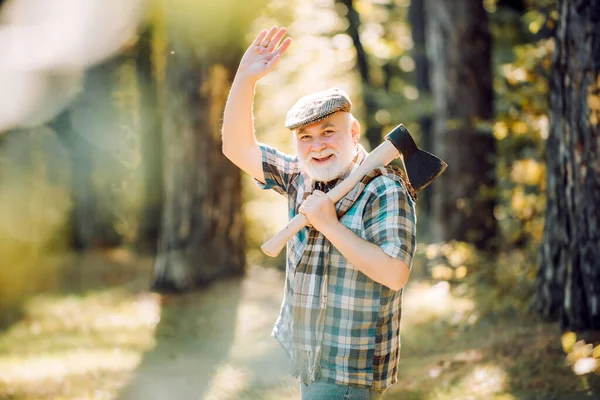 Smiling man with axe. Rest in forest. Outdoor portrait. Old bearded male. Elderly male walk in forest. Old hipster man. Bearded man relax in forest. Hiking in deep wood. — Stock Photo, Image