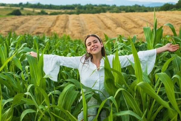 Femme fermière joyeuse posant dans la récolte de maïs. Jeune fille heureuse montrant le maïs récolté dans le champ. — Photo