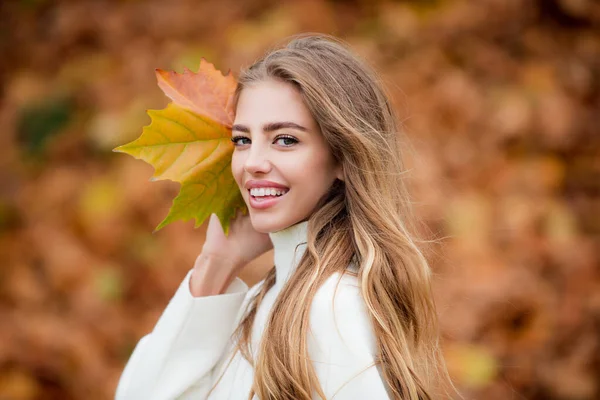 Glücklich lächelnde Frau hält gelbe Ahornblätter vor herbstlichem Hintergrund in den Händen. — Stockfoto